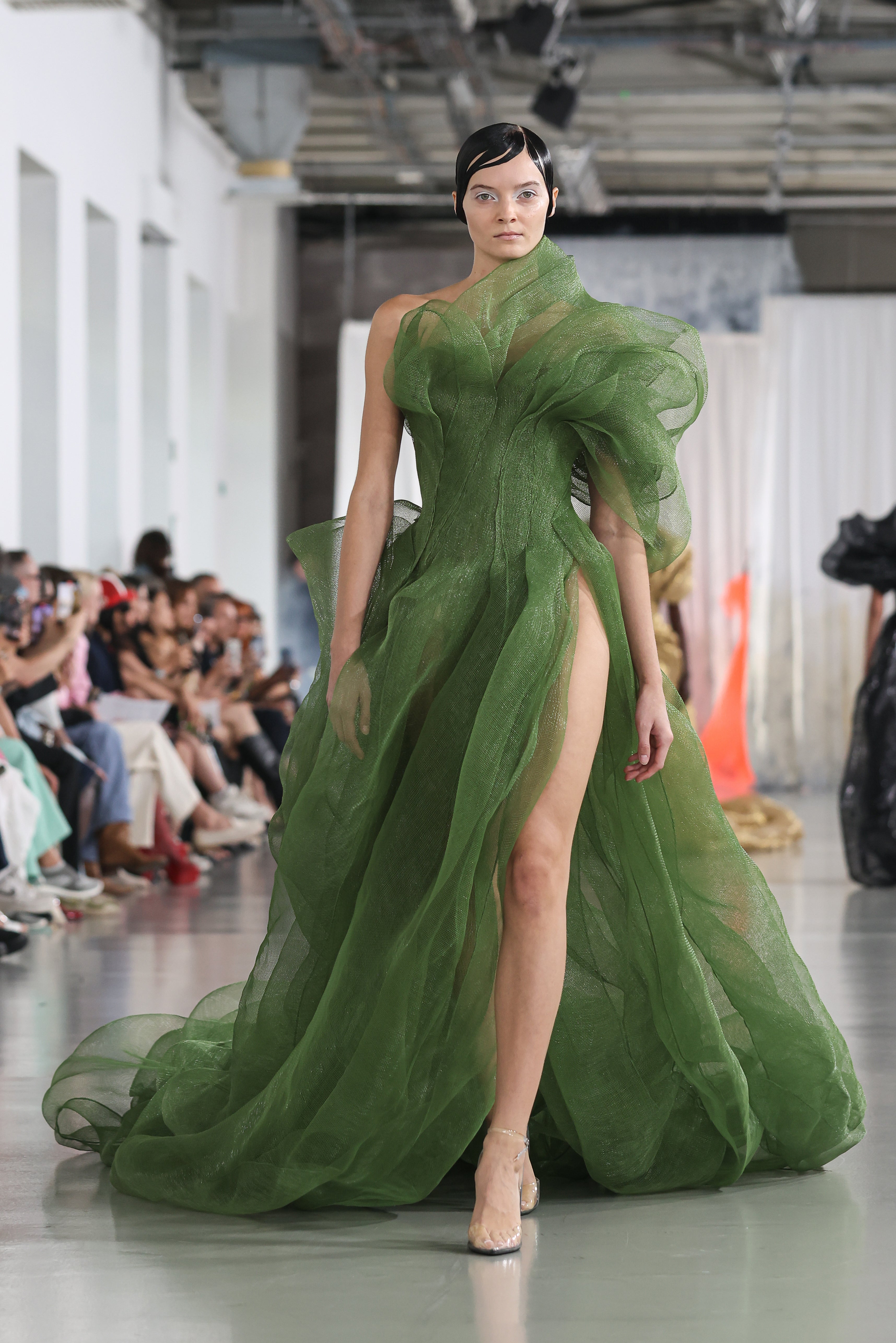 Model wearing fitted green couture dress with puffy elbow-length sleeves and high slit