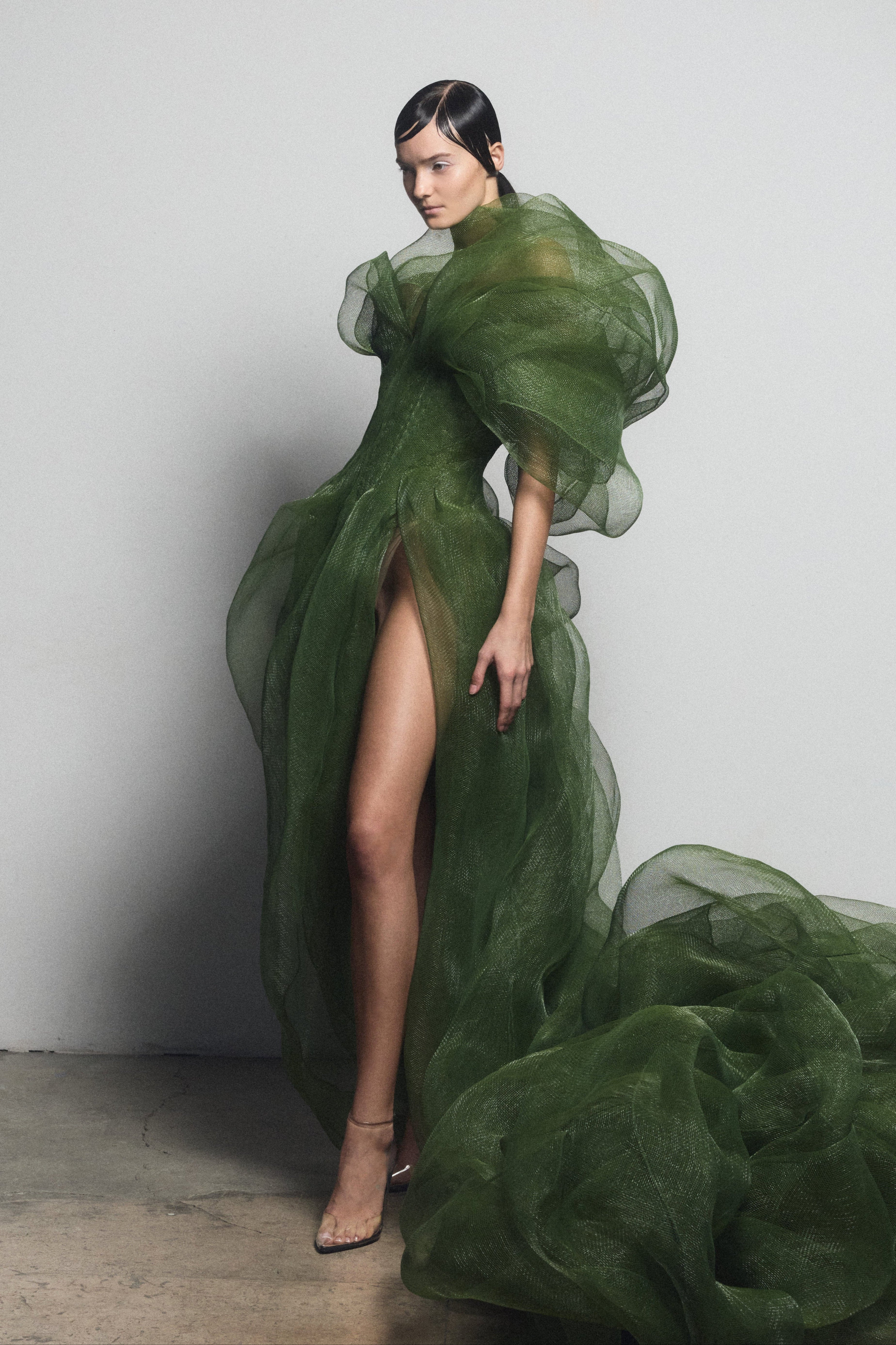 Model wearing fitted green couture dress with puffy elbow-length sleeves and high slit